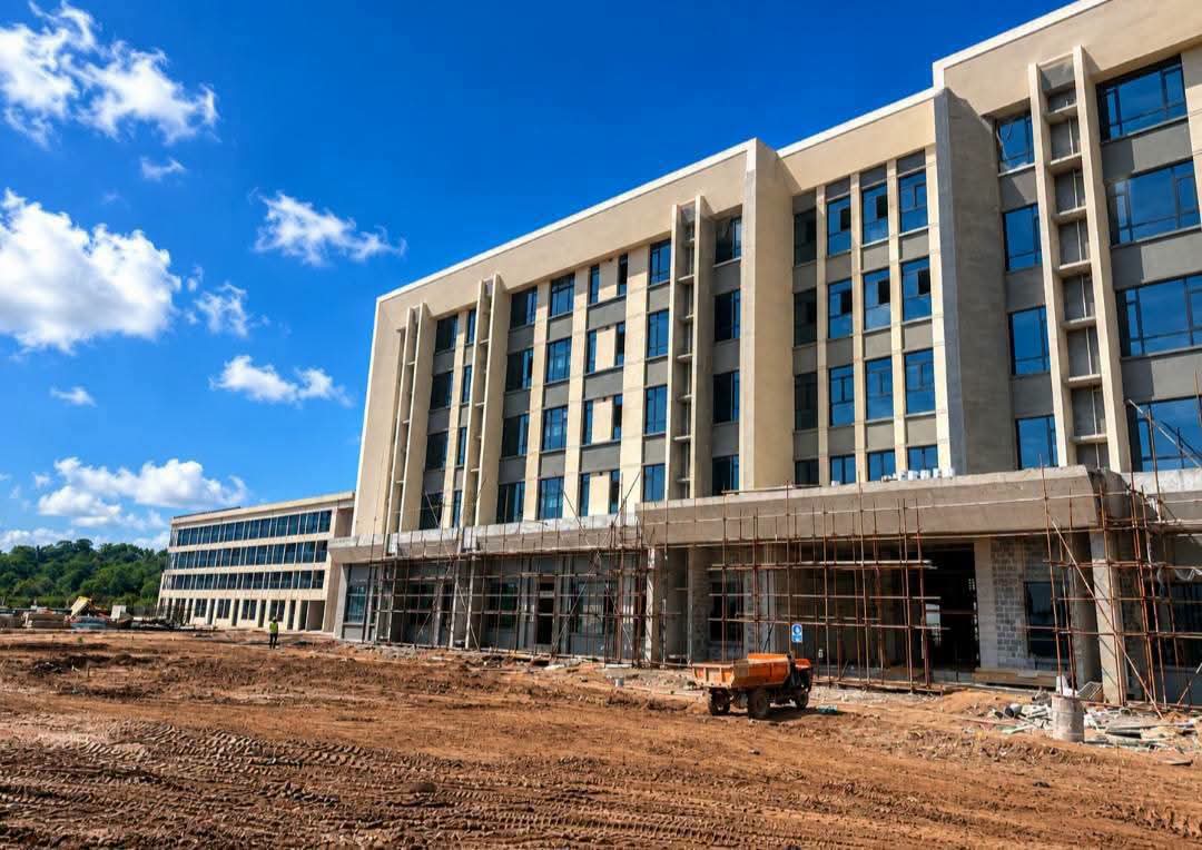 Low-angle perspective of a modern multi-story commercial building under final construction with scaffolding and red earth in the foreground.